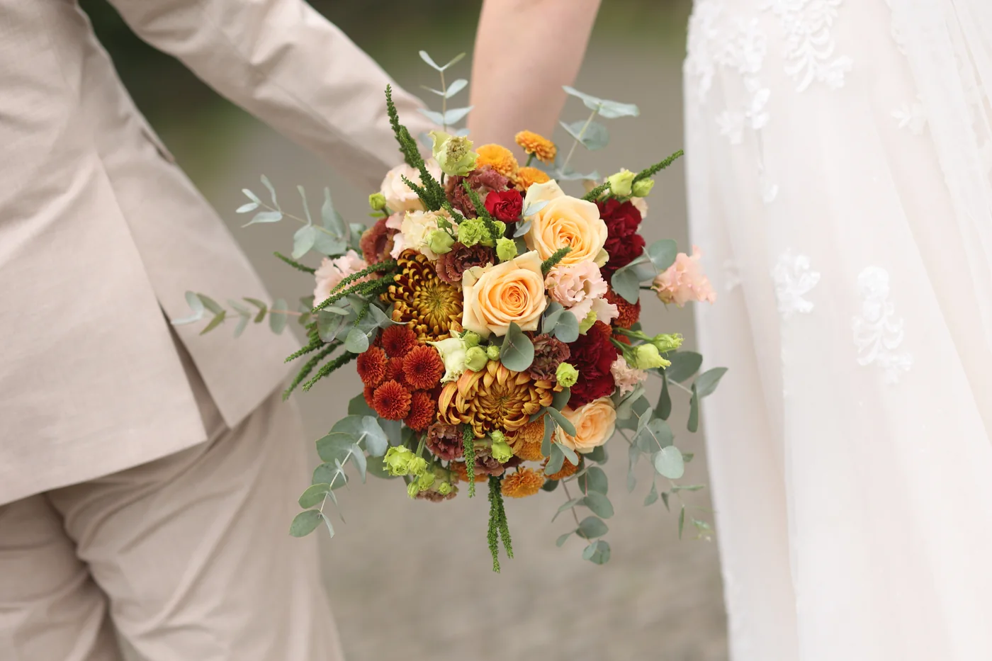 Herbstlicher Brautstrauß in Jennifers Händen zwischen Brautkleid und hellem Anzug